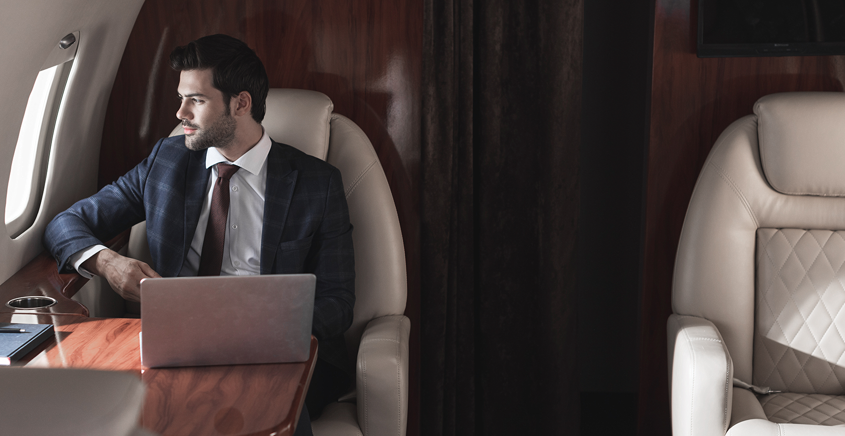 Serious man in tuxedo seated on a plane, with a black cellphone to his ear