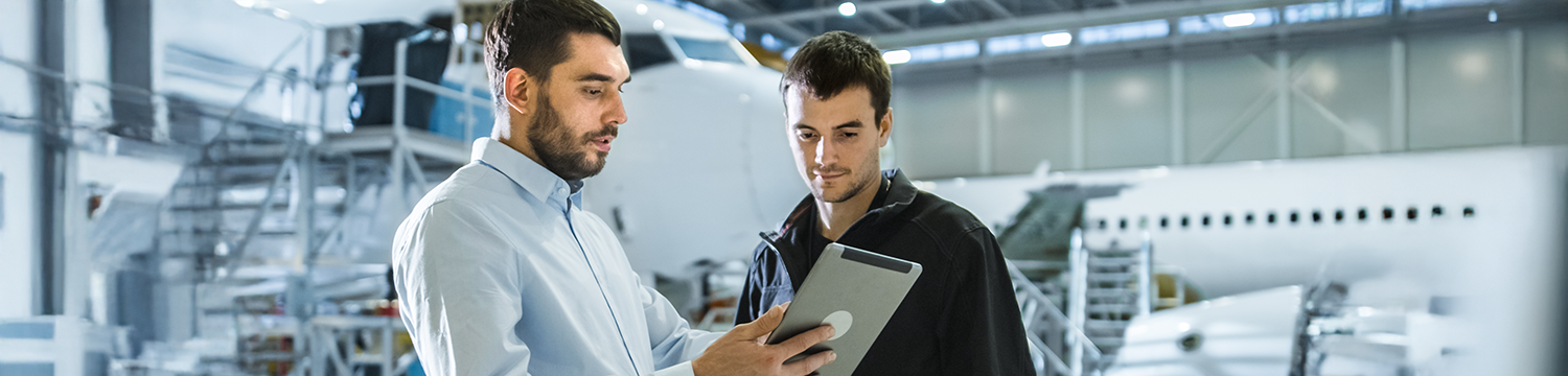 Two men inside hangar looking at tablet