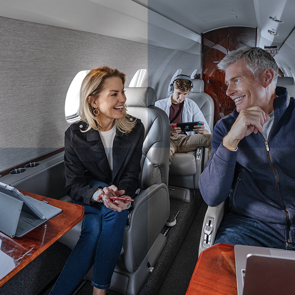 Uma família de três pessoas viajando de avião, usando tablet, telefone e console de jogos