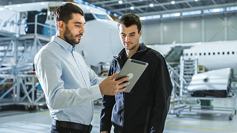 Dois homens dentro de hangar olhando para tablet